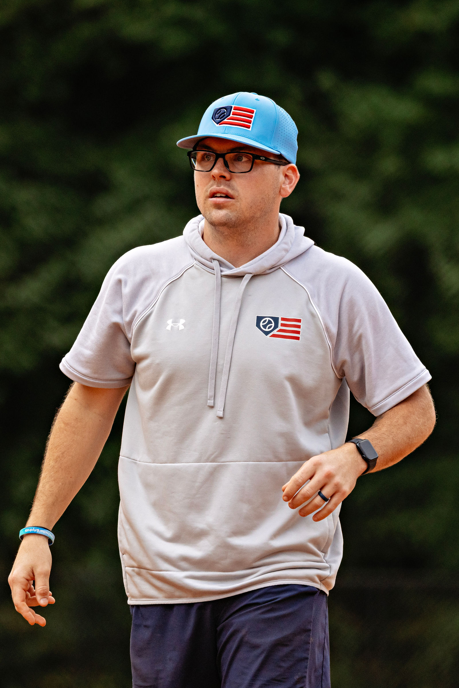 Coach Ryan Dudney on the field wearing a Revolution cap and gray hoodie.